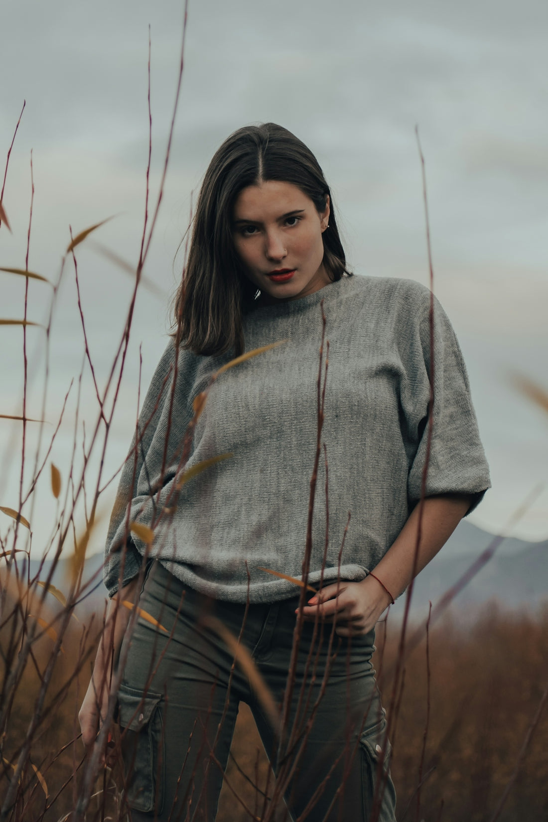 woman in gray knit shirt and brown plaid pants standing on grass field during daytime