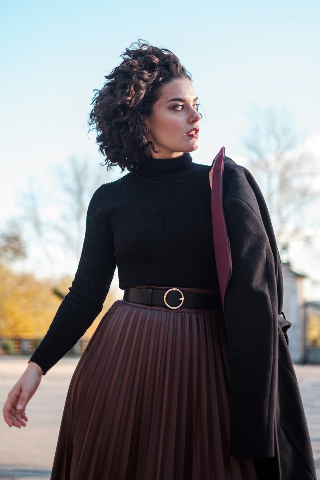 a woman wearing a brown pleated skirt and a black sweater