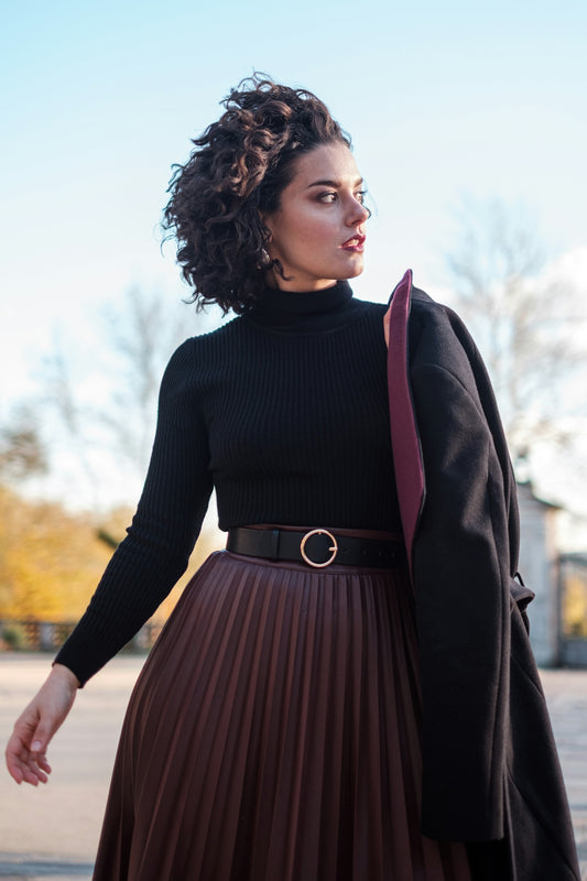 a woman wearing a brown pleated skirt and a black sweater