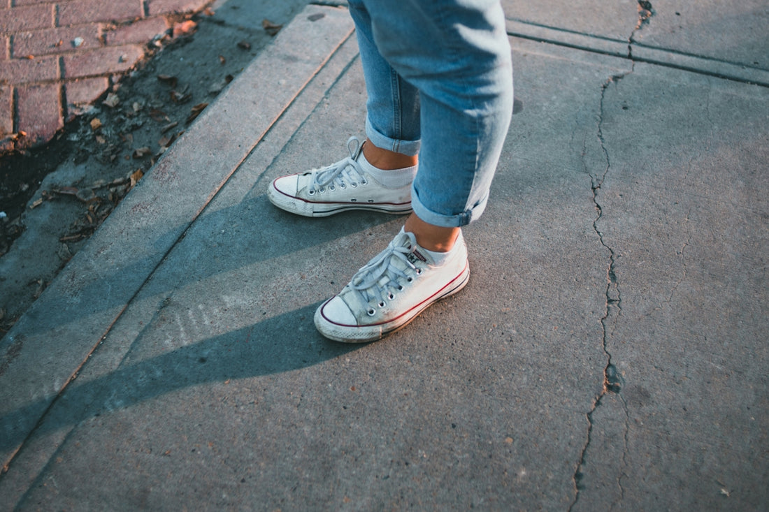 a person standing on a sidewalk wearing white sneakers