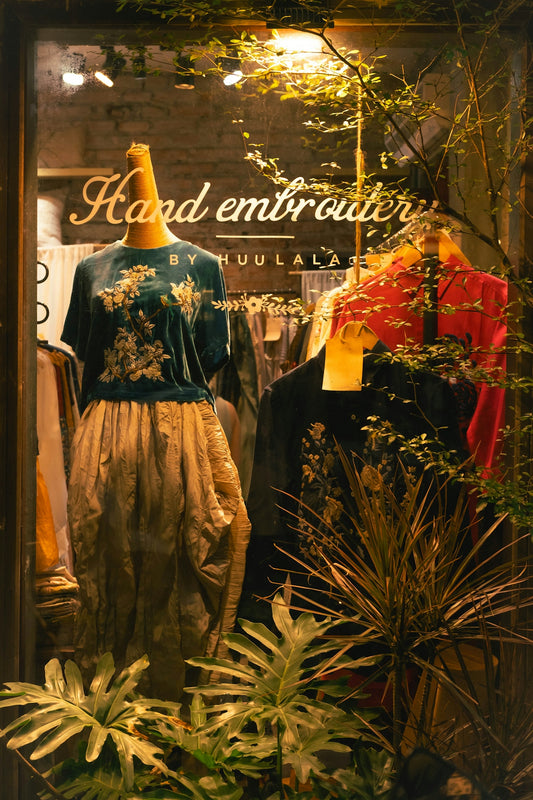Shop window displays embroidered clothing and greenery.