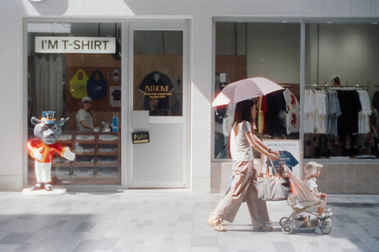 Woman pushes stroller past a t-shirt shop.