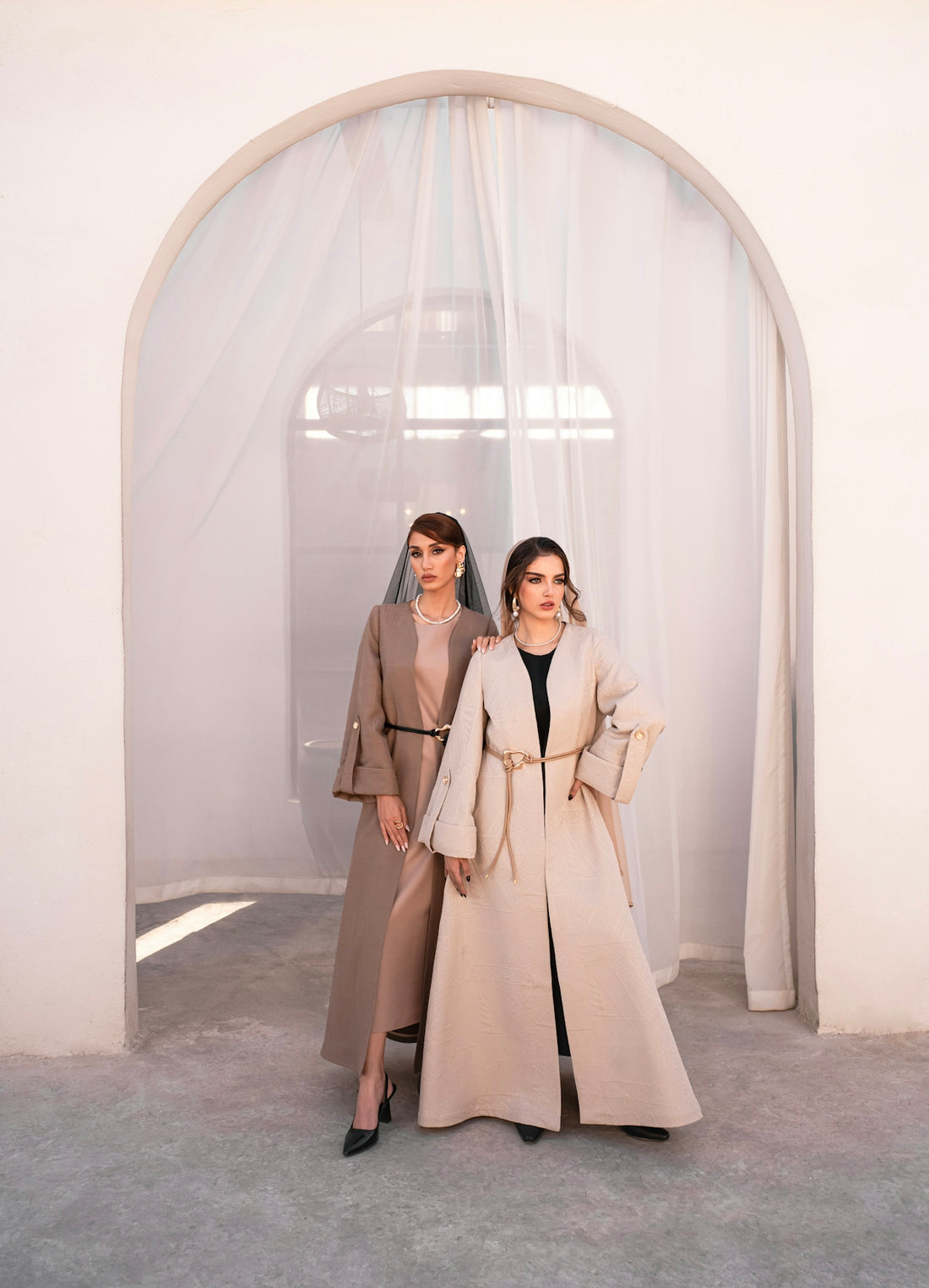 Two women in elegant abayas standing indoors