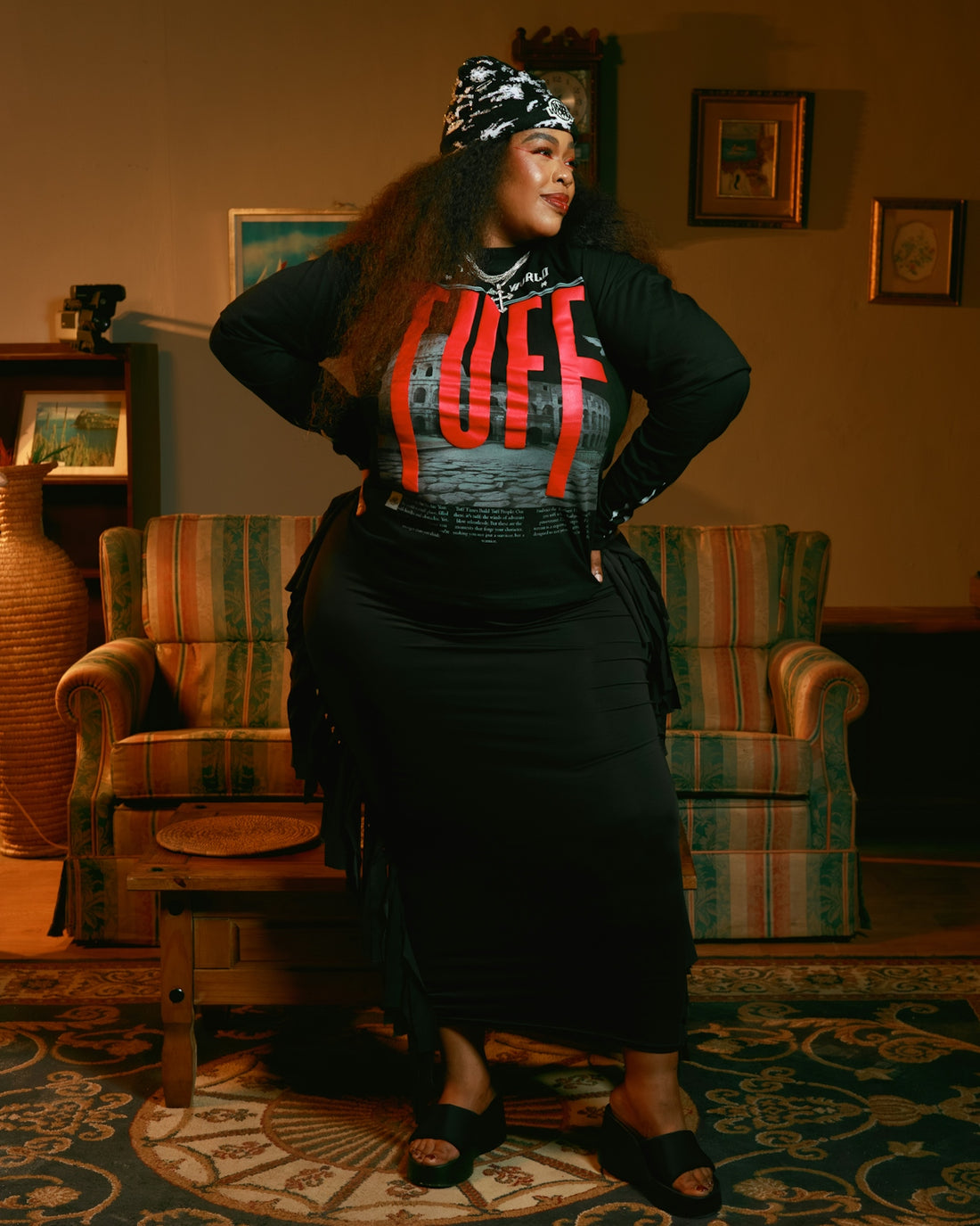 Woman in black dress and bandana poses indoors