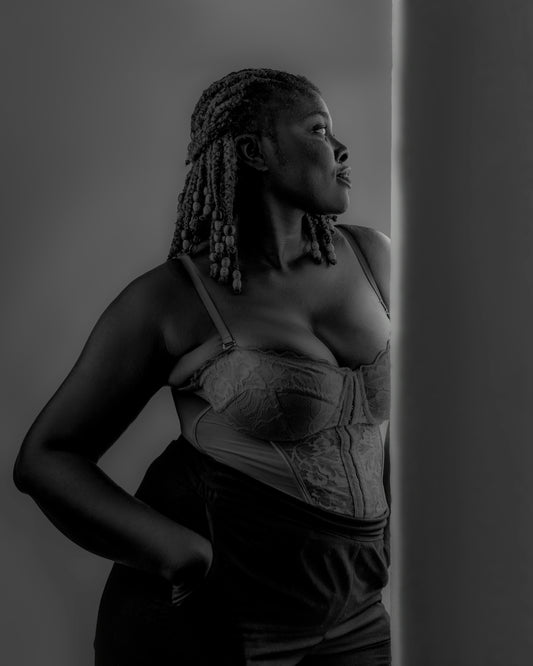 A black woman in a corset looks out a window