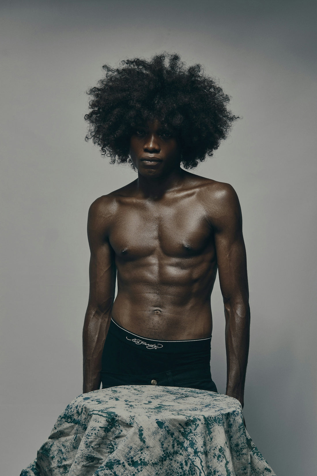 Muscular man with afro standing shirtless, looking at the camera.