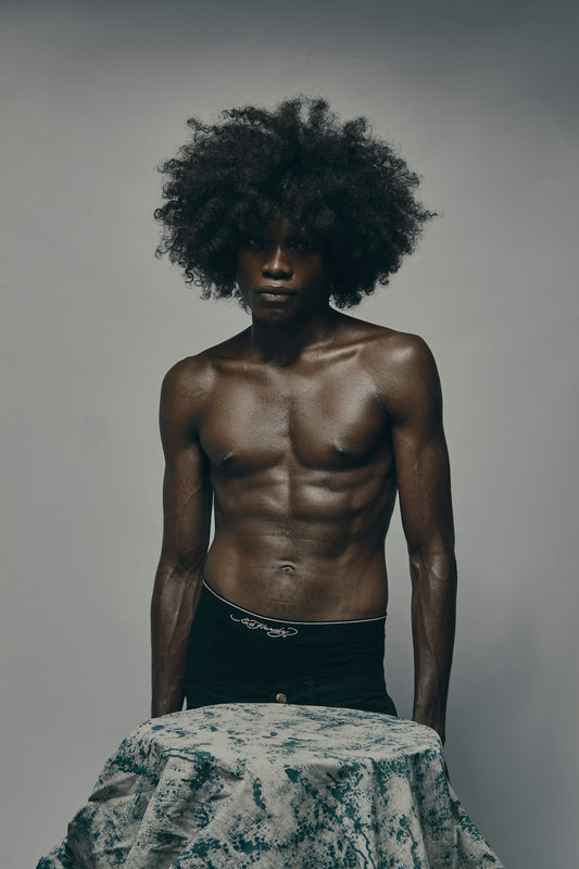 Muscular man with afro standing shirtless, looking at the camera.